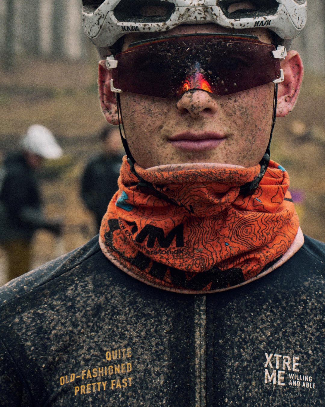 A muddy cyclist at a gravel race. Wearing muddy Willing Able Xtreme clothing while smiling at the camera