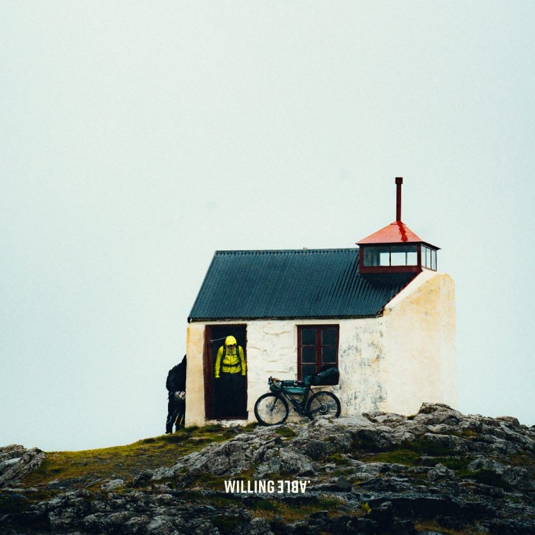 A house in Iceland with a bike in front of it, and the text Willing Able written on the ground in front of the house and bike.