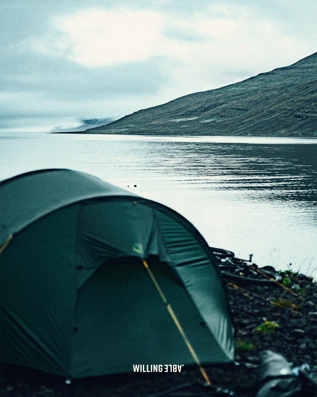 a tent put up in iceland next the sea with a view of a mountain.
