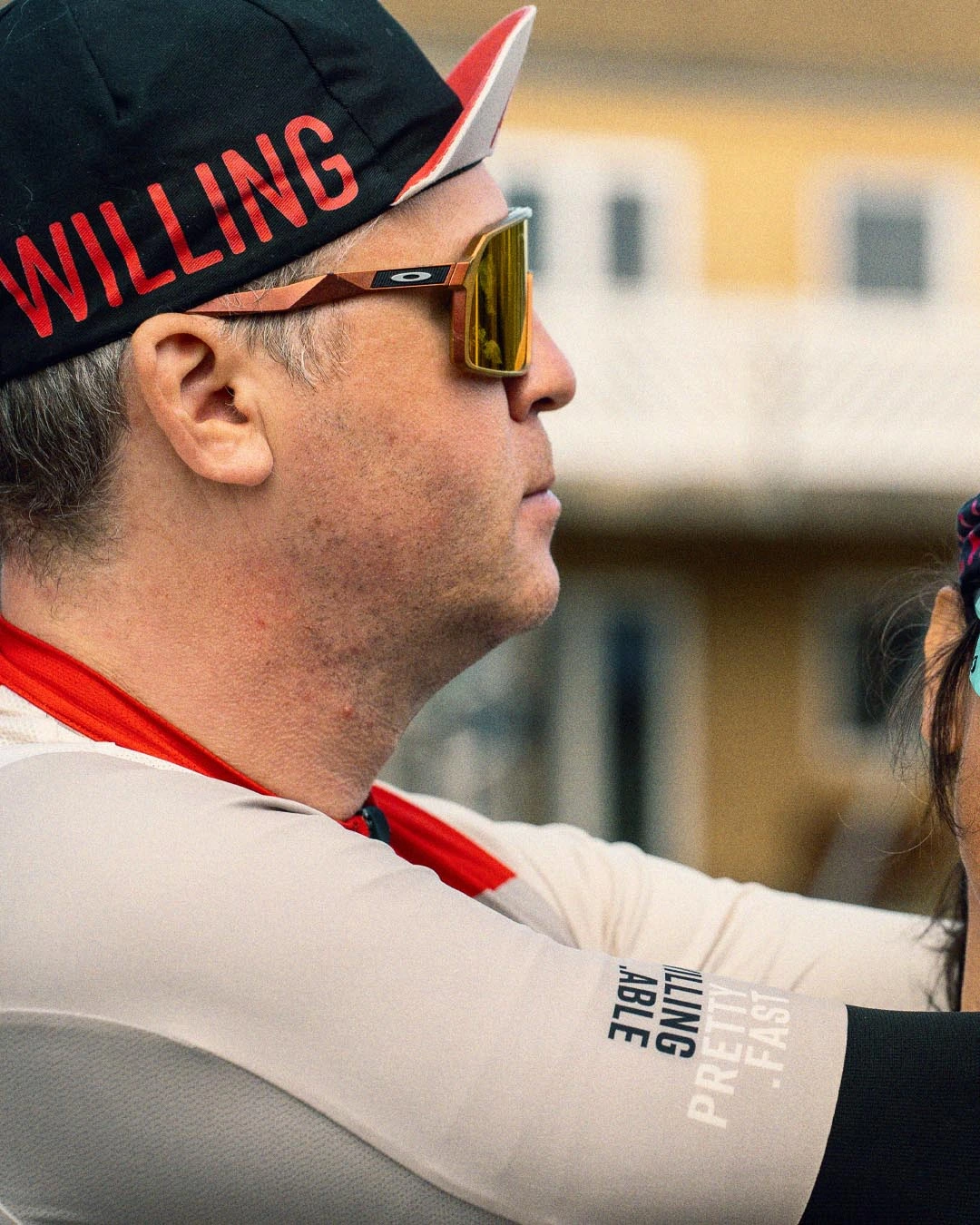 Close-up of Michael Dvinge, the inspiring founder of Tour De Jutland for people with disabilities, hugging his fellow cyclist. He is wearing Willing Able clothing and a cap.