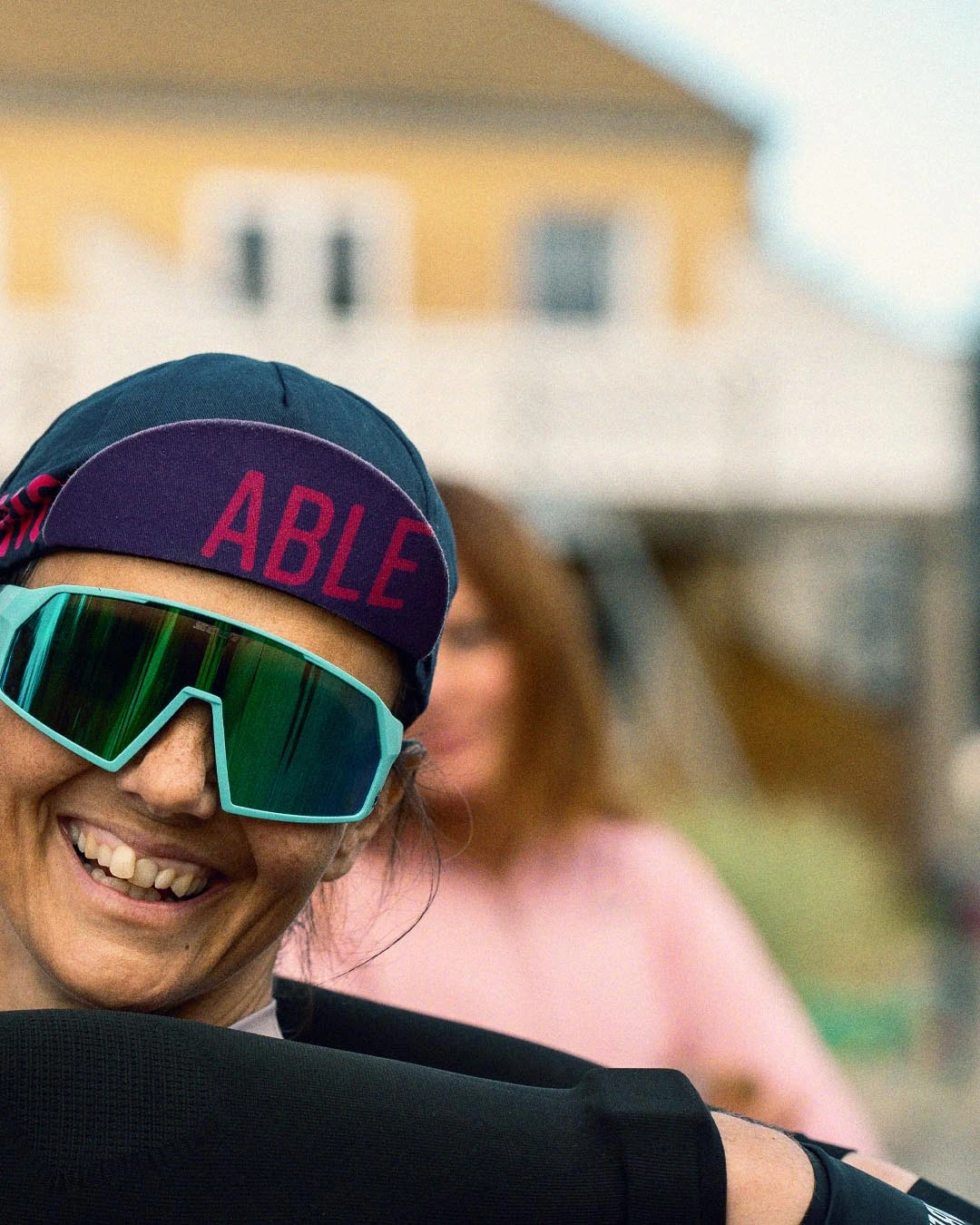 Female cyclist being hugged by Michael Dvinge. She is smiling broadly and wearing Willing Able clothing and a cap. They both inspire people with disabilities.